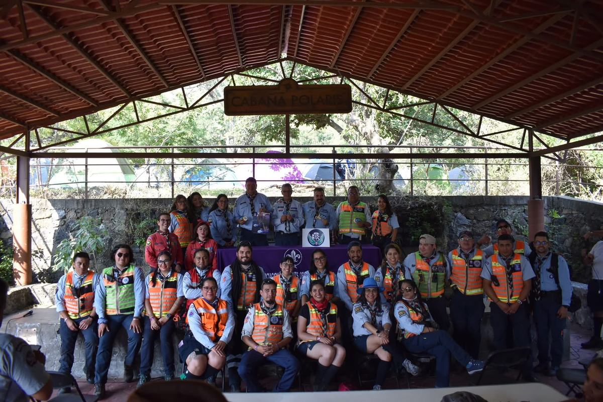 Grupo numeroso de scouts con chalecos de colores reunidos bajo un techado